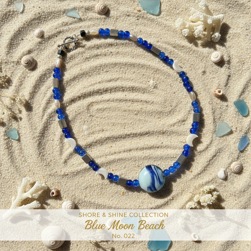 Cobalt blue crackle glass beaded necklace with moon charms and art glass focal bead on sand surface