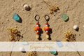 Guppie Drups goldfish dangle earrings on coastal flat lay with shells and sea glass