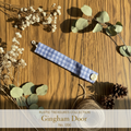 Blue gingham plaid wrist wrap with cream rose button on weathered wood surface